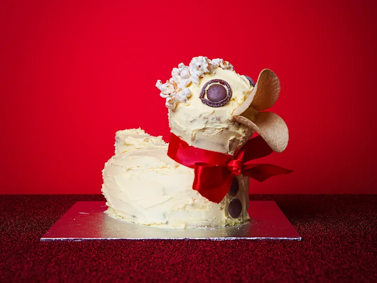 A duck-shaped cake with pale yellow frosting and a red ribbon