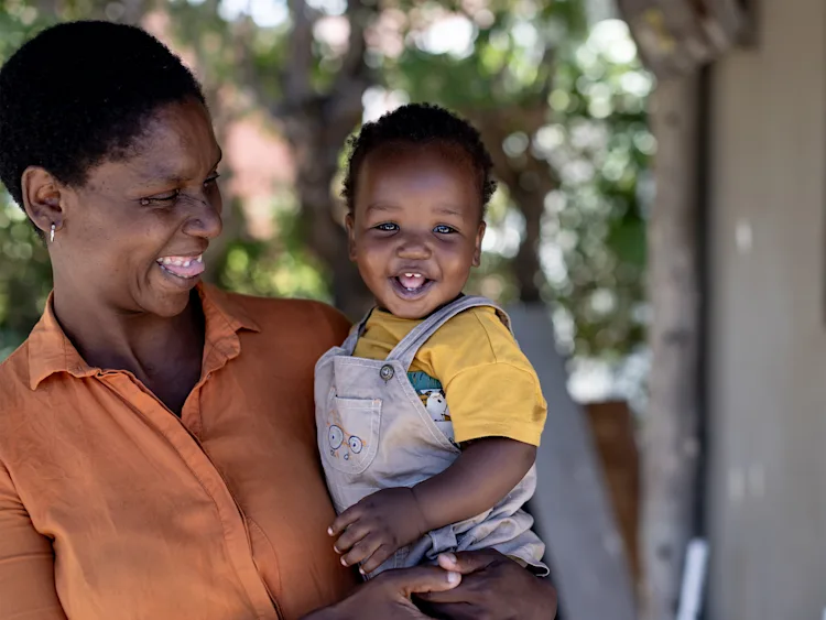 Woman holding a toddler in her arms who is smiling at the camera
