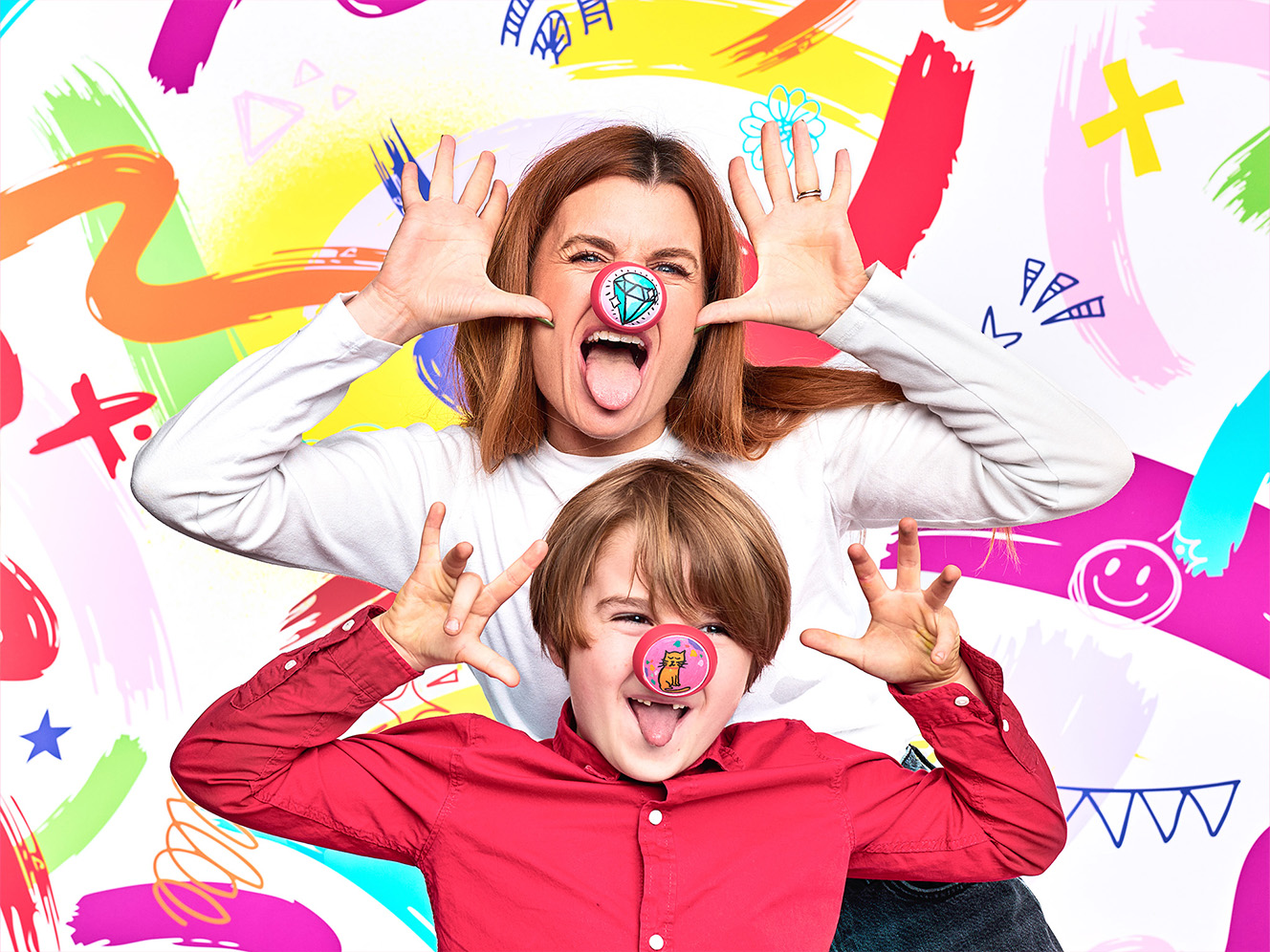 Two playful individuals pose against a vibrant, colourful background, making funny hand gestures with smiles