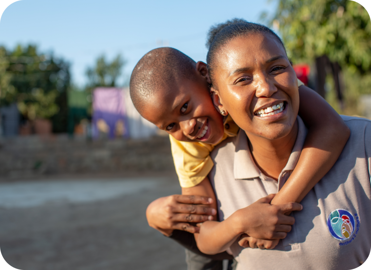 a children's care worker smiling and laughing with a child she's carrying on her back.