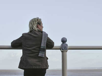 Kate leans on a handrail and looks out to the open sea.