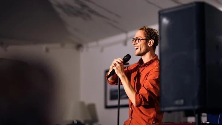 A man performs comedy onstage at the Alverbank.