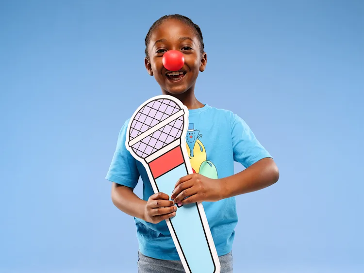 A child wearing a red nose holding a paper microphone