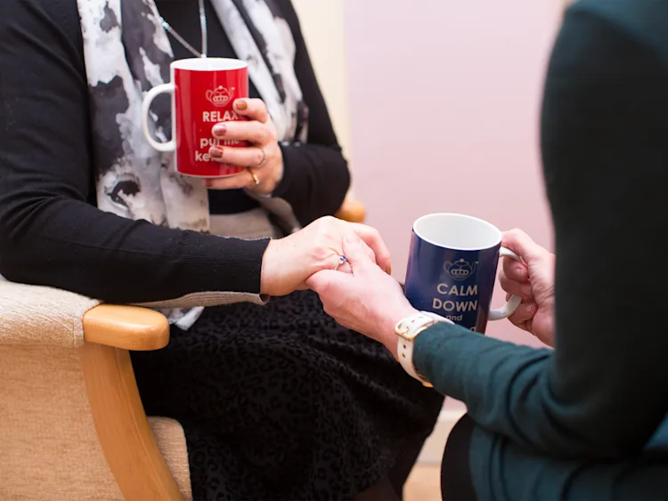 Two people holding hands and holding a mug of tea.