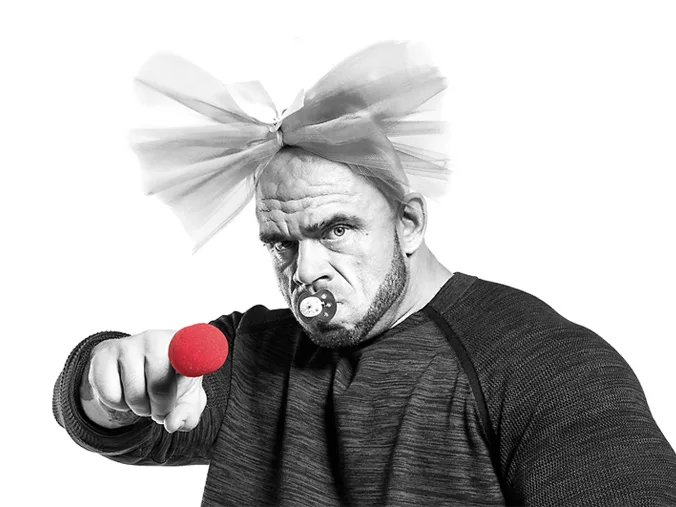 Nose Day, Finland, Bald muscly guy with a bow in his hair, dummy in his mouth and a red nose on his pointing finger