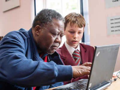 A school pupil helping an elderly man use a computer