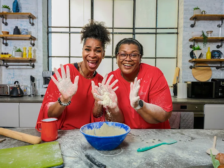 Two women wearing red t-shirts with a baking bowl and baking accessories in front of them