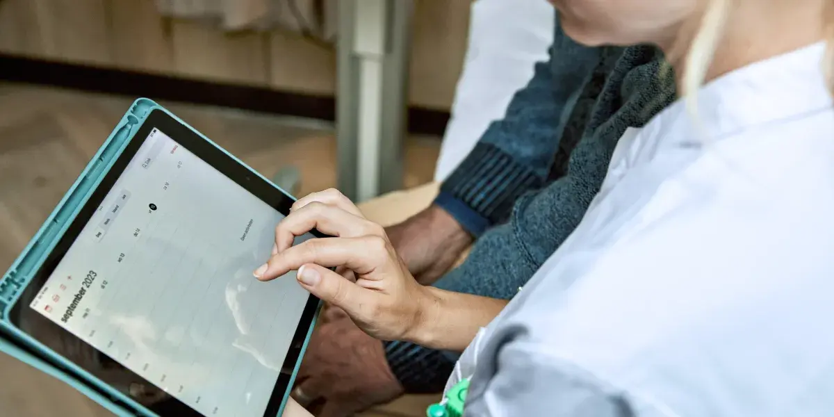 Een arts en patiënt zitten samen in bespreking met een tablet.