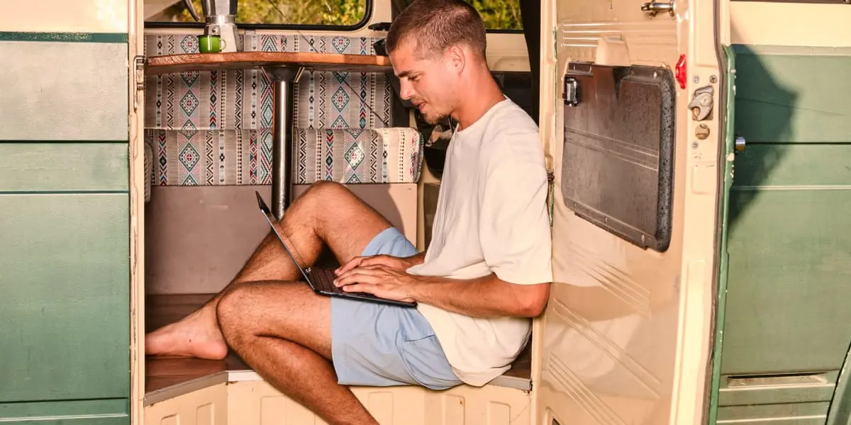 Man met laptop op schoot in caravan van de zijkant 