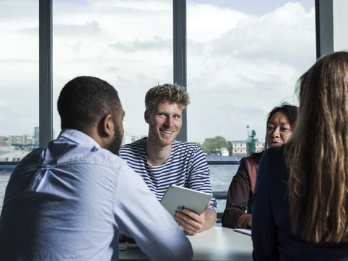 Een groep mensen vergadert. Een medewerker lacht naar een van de collega's. 