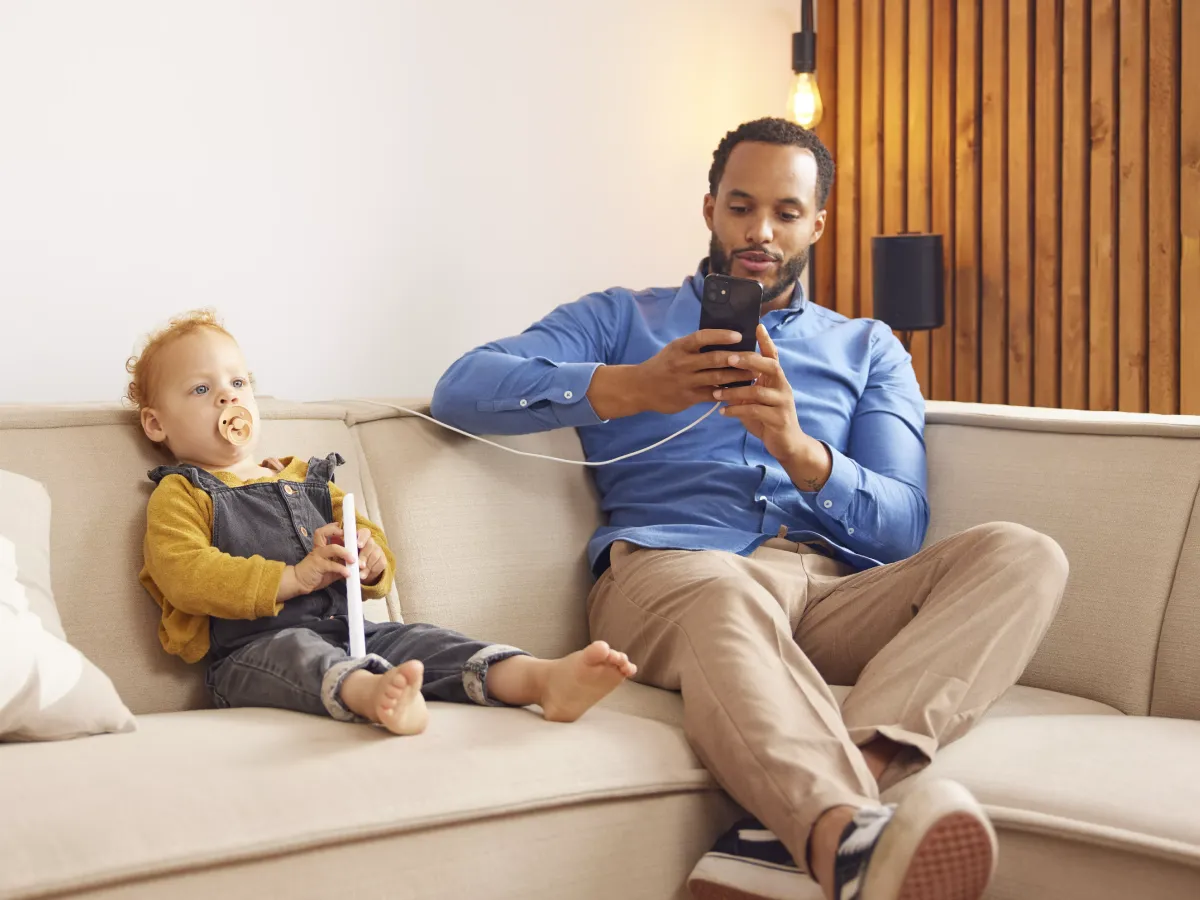 Man met telefoon zit op de bank met kind