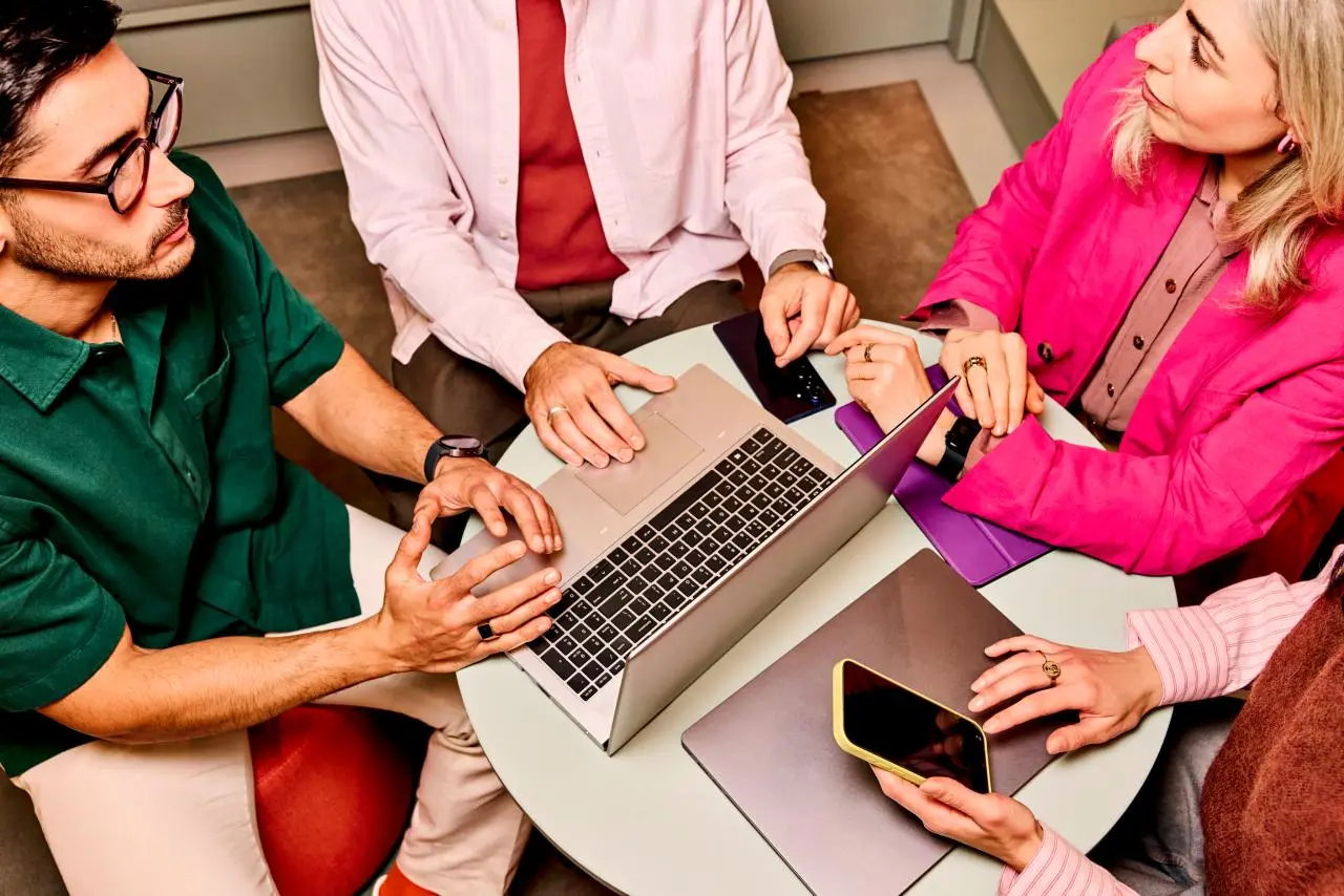 Sfeer: Groep mensen in overleg aan tafel met laptop en telefoon. Beeld van boven. 