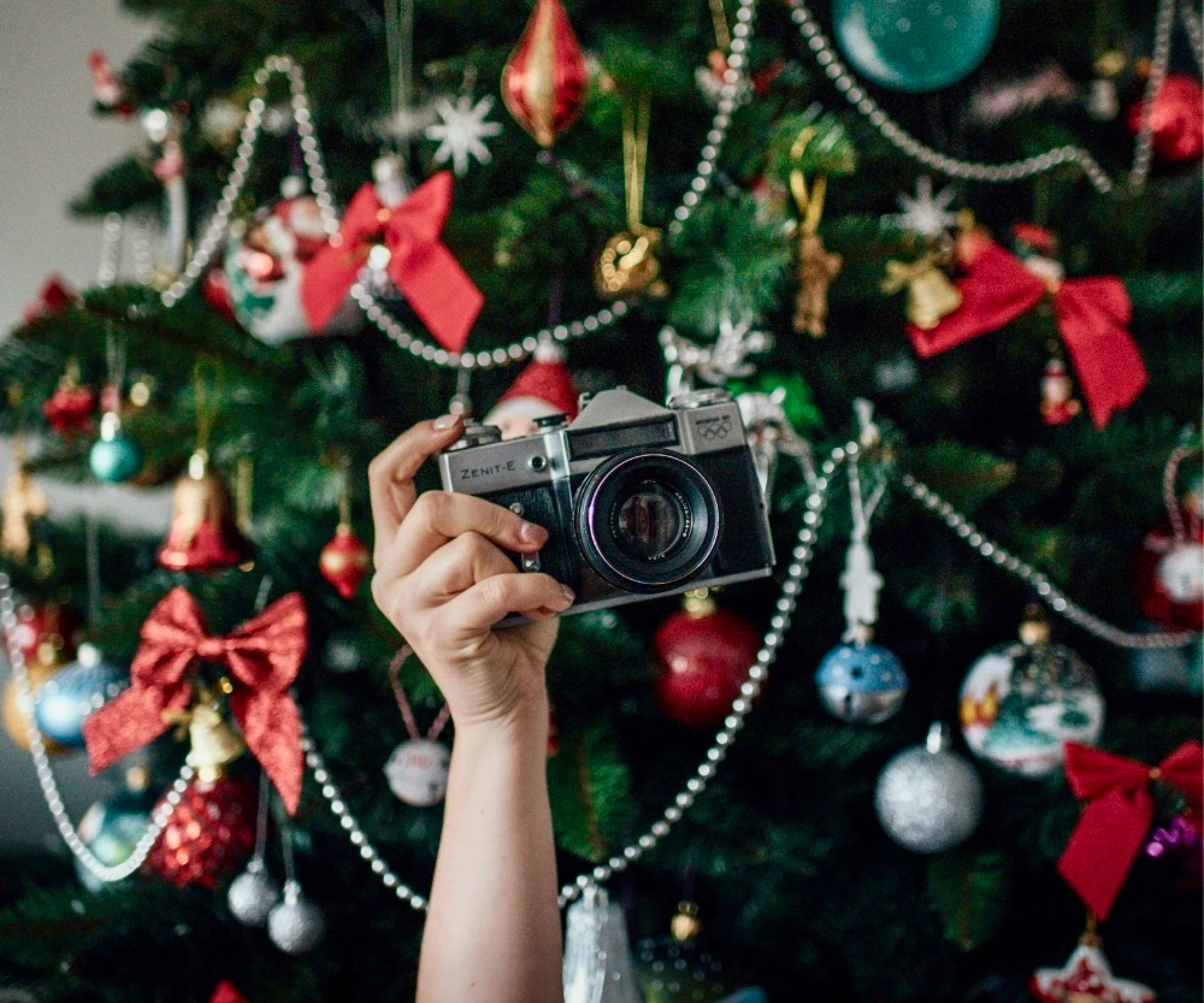 Een hand met een analoog fototoestel en een kerstboom op de achtergrond