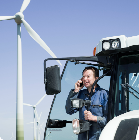 Meneer belt en kijkt in de verte. Op de achtergrond draaien de windmolens.