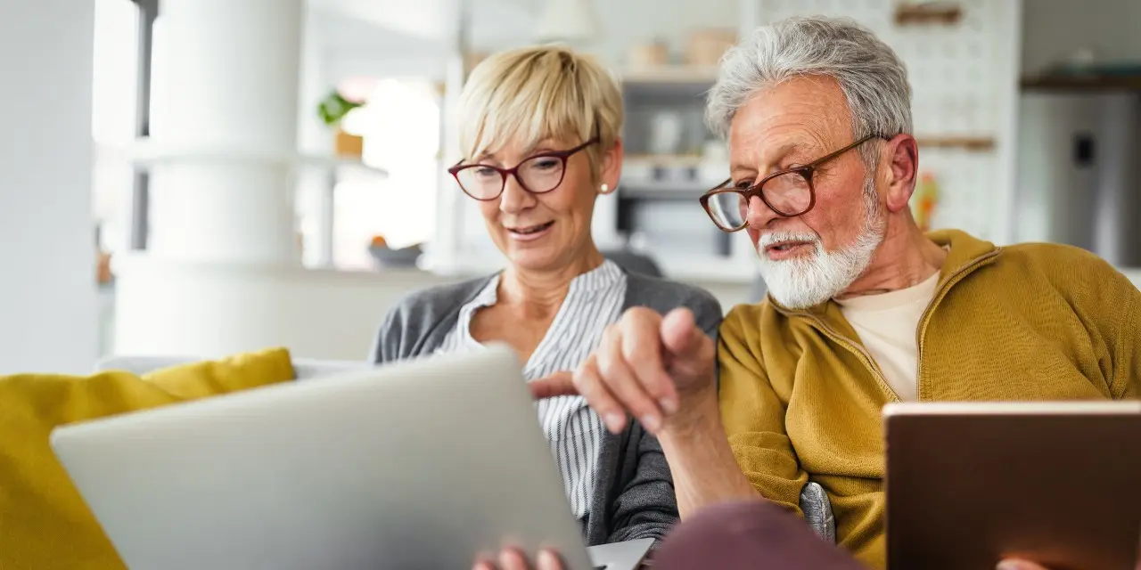 Een wat meer op leeftijd stel zit op de bank en kijken naar beeldschermen van laptops