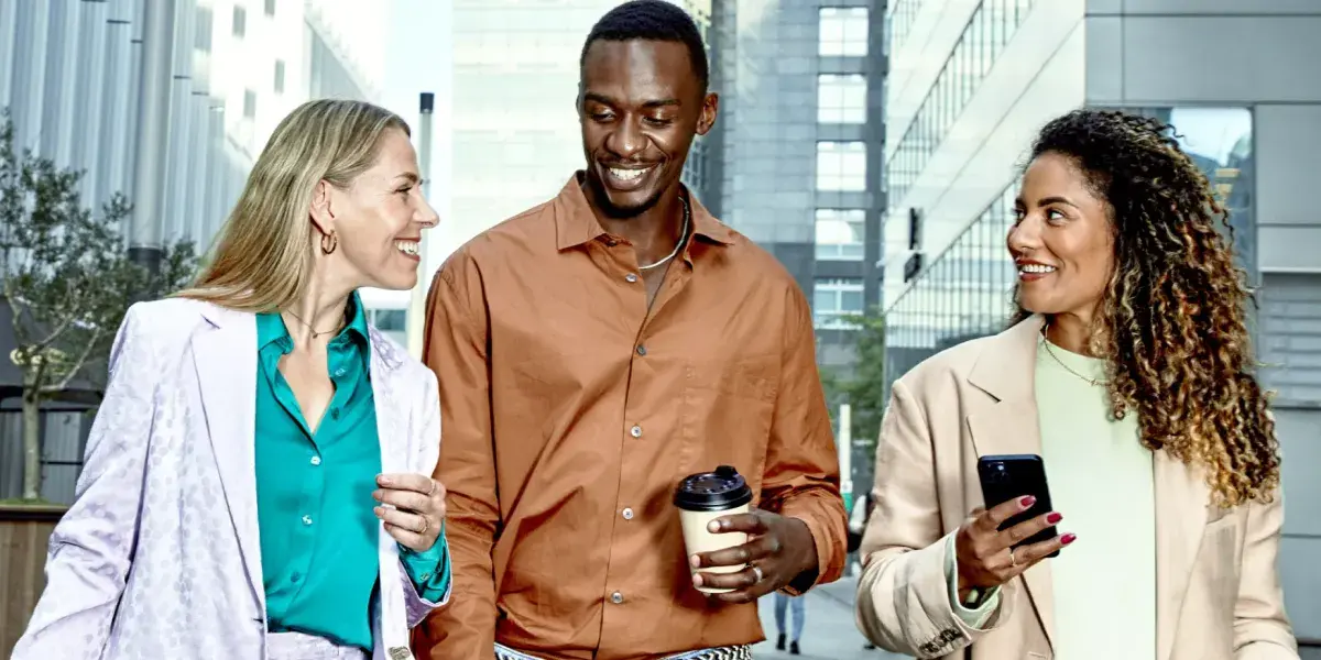 Drie collega's lopen buiten met koffie en smartphone in de hand