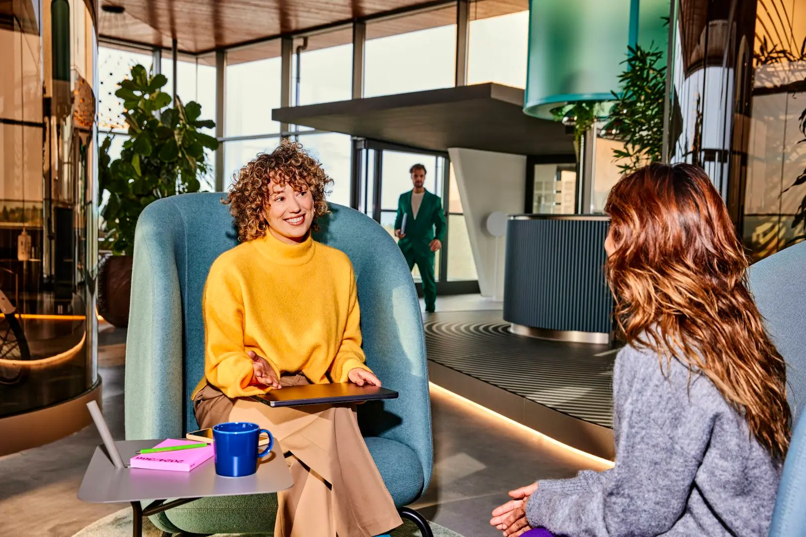 Twee medewerkers praten met elkaar. Op de achtergrond loopt een medewerker naar binnen