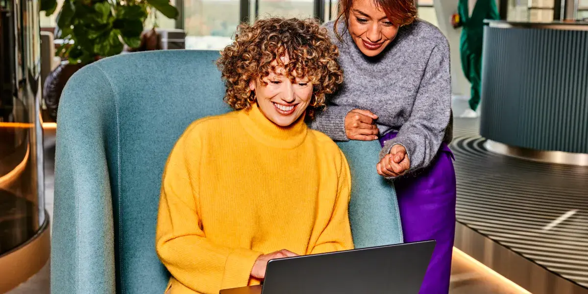 Twee vrouwelijke collega's kijken op laptop. Een dame zit en de andere staat achter de stoel