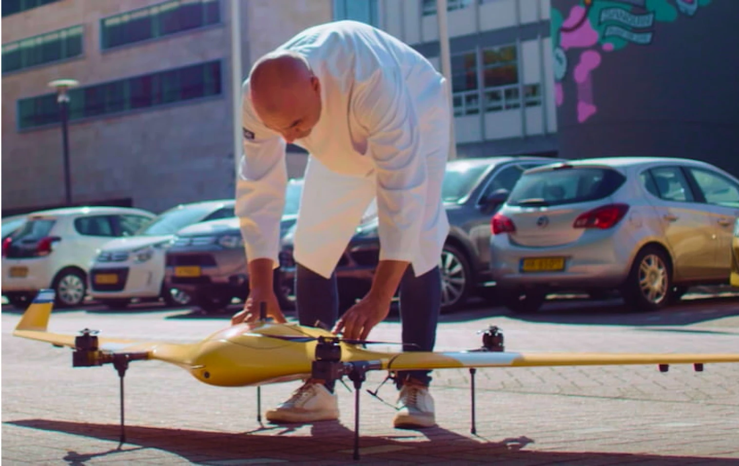 Man in witte labjas legt zijn handen op een drone op de grond