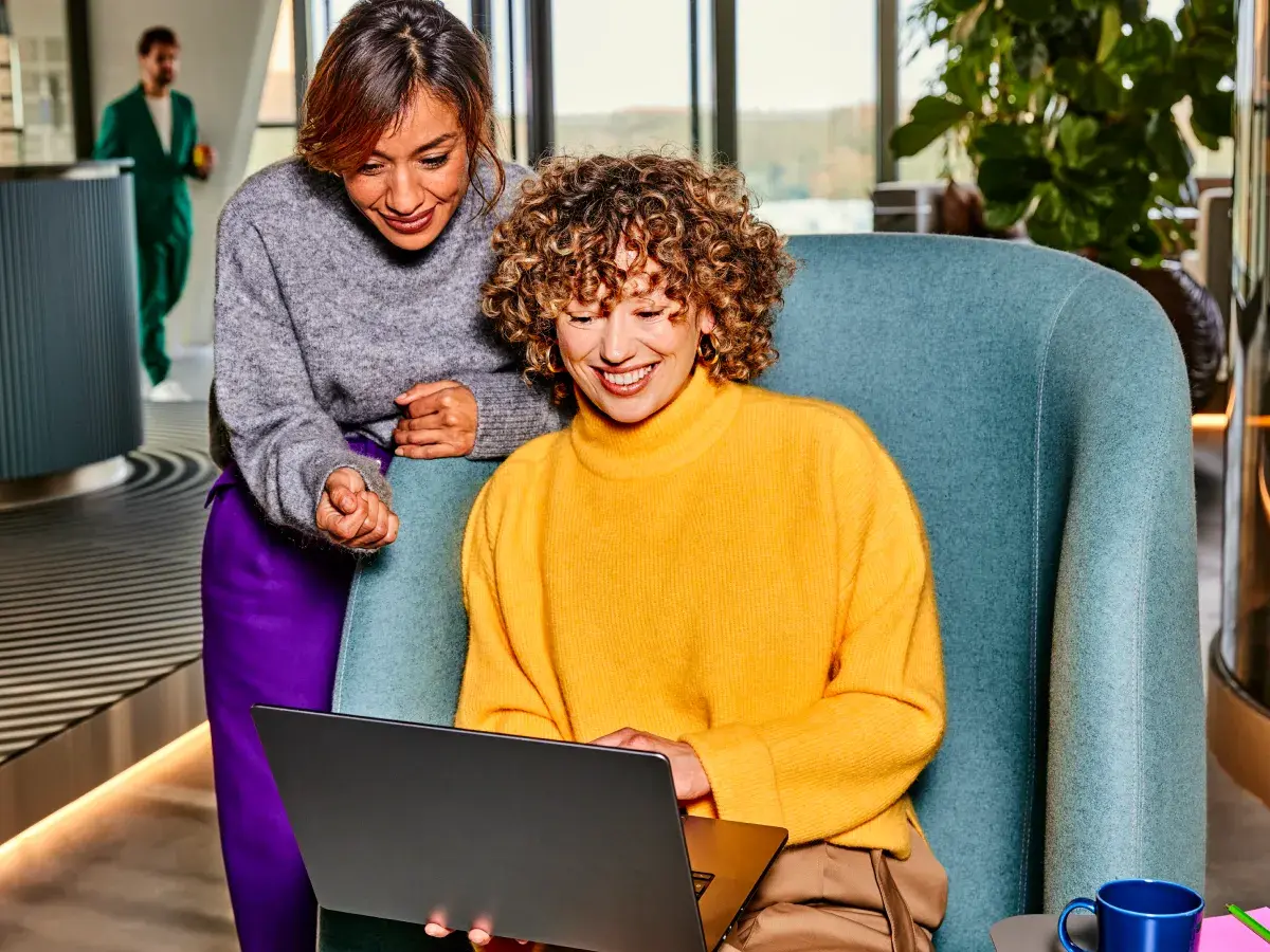 Twee vrouwelijke collega's in overleg met een laptop. Een collega staat, de andere zit op een stoel.