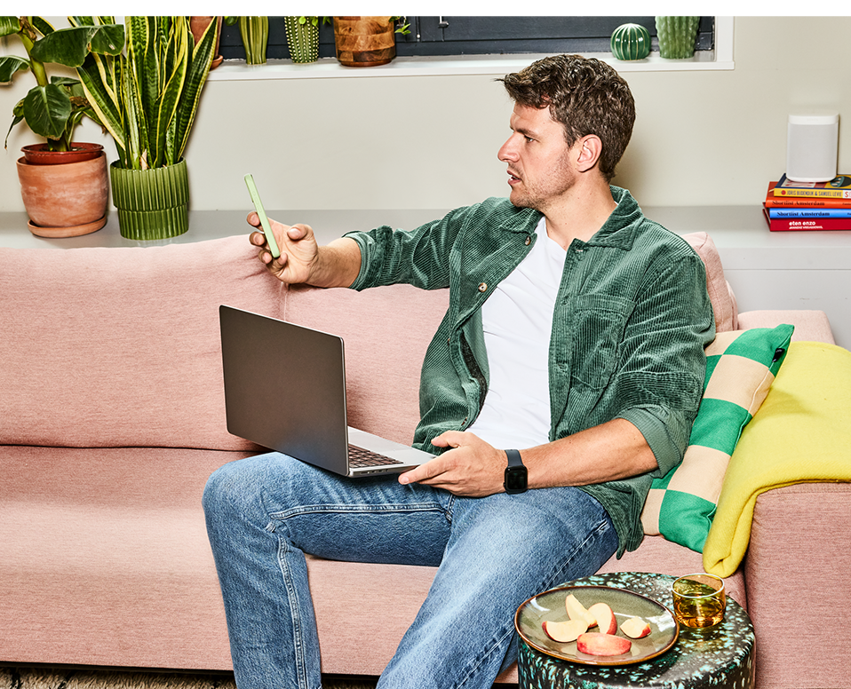 Man zit op de bank met laptop en mobiel