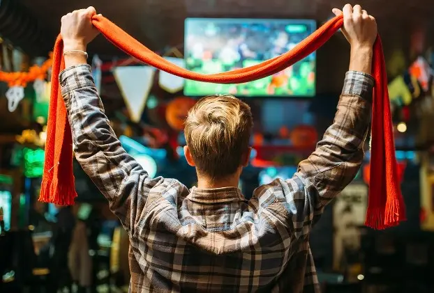 Man houdt oranje sjaaltje vast en kijkt voetbal