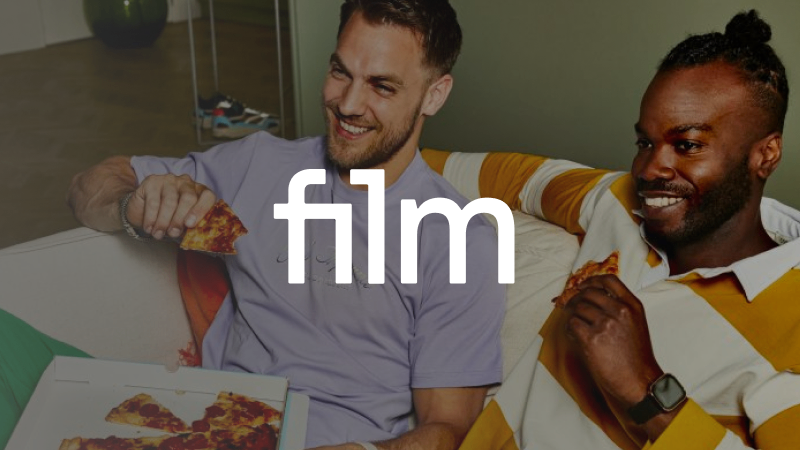 Film1 logo met op de achtergrond twee mannen die op de bank zitten, een film kijken en pizza eten