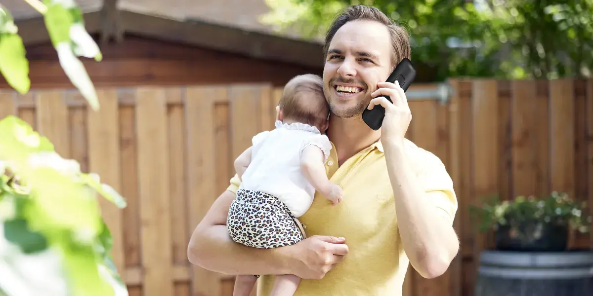 Een man belt in zijn tuin. Op zijn arm houdt hij een baby vast.