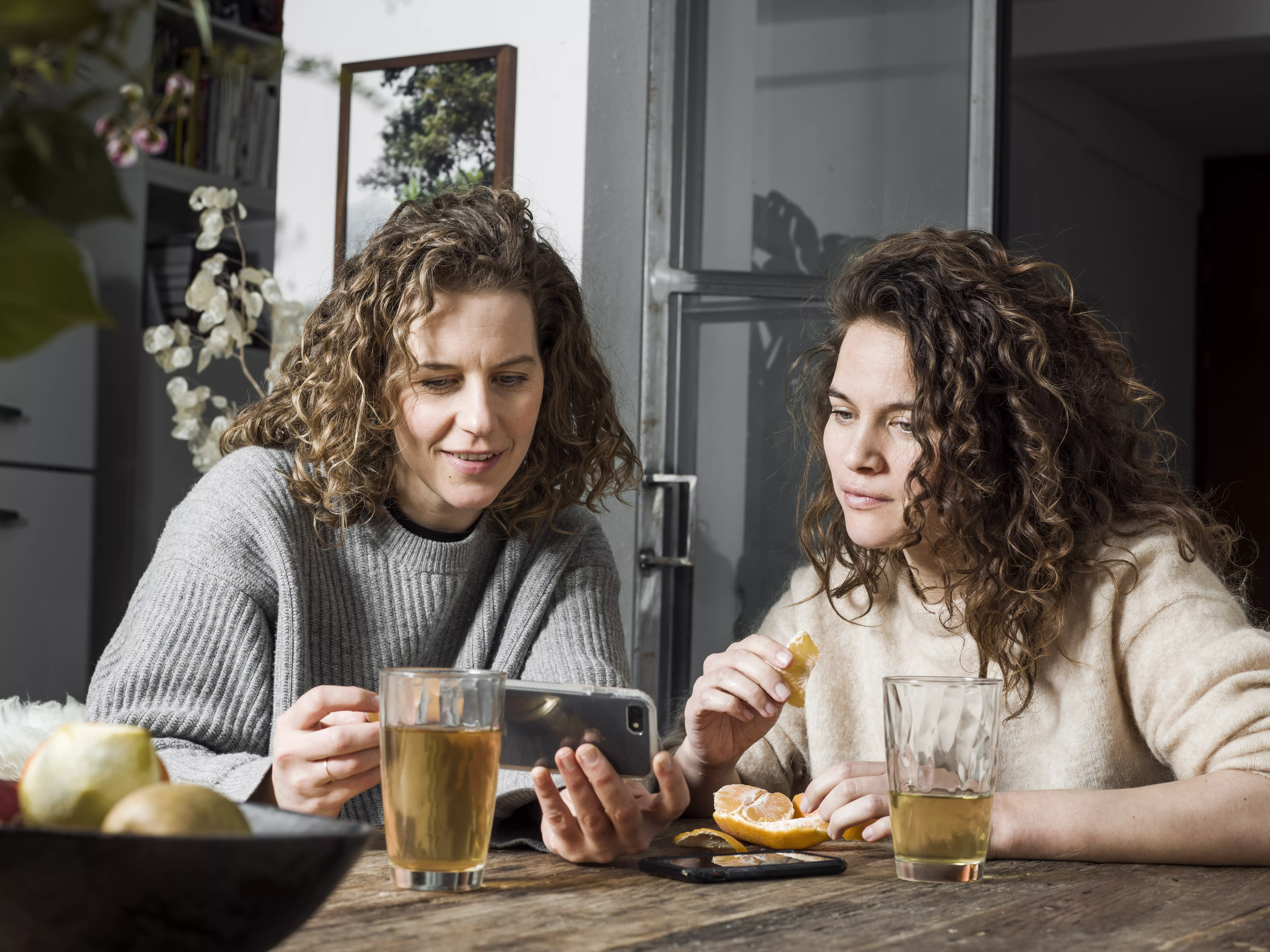 2 vrouwen kijken op een mobiele telefoon aan tafel met kopje thee