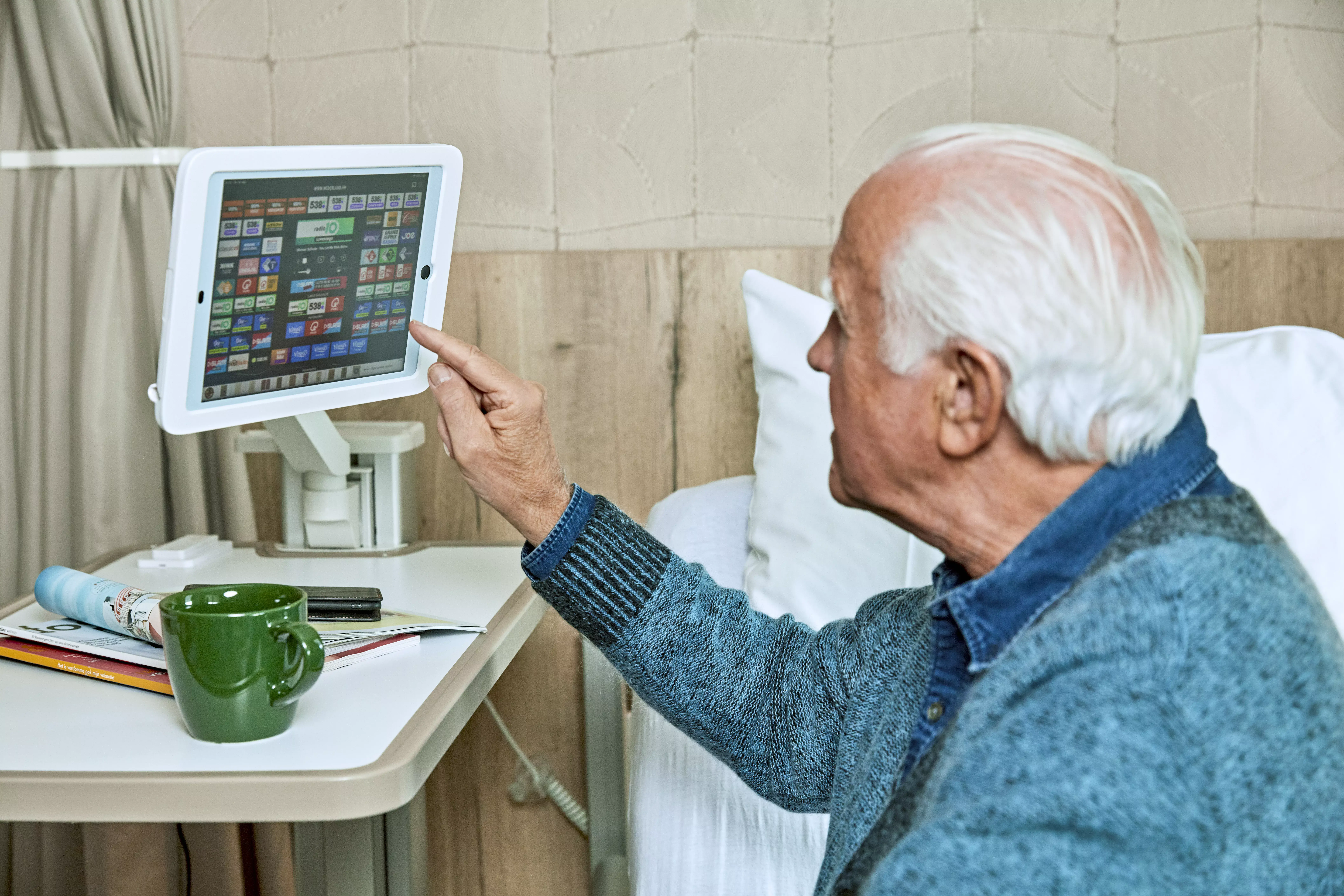 Oudere man zit op een ziekenhuisbed en kijkt naar een monitor