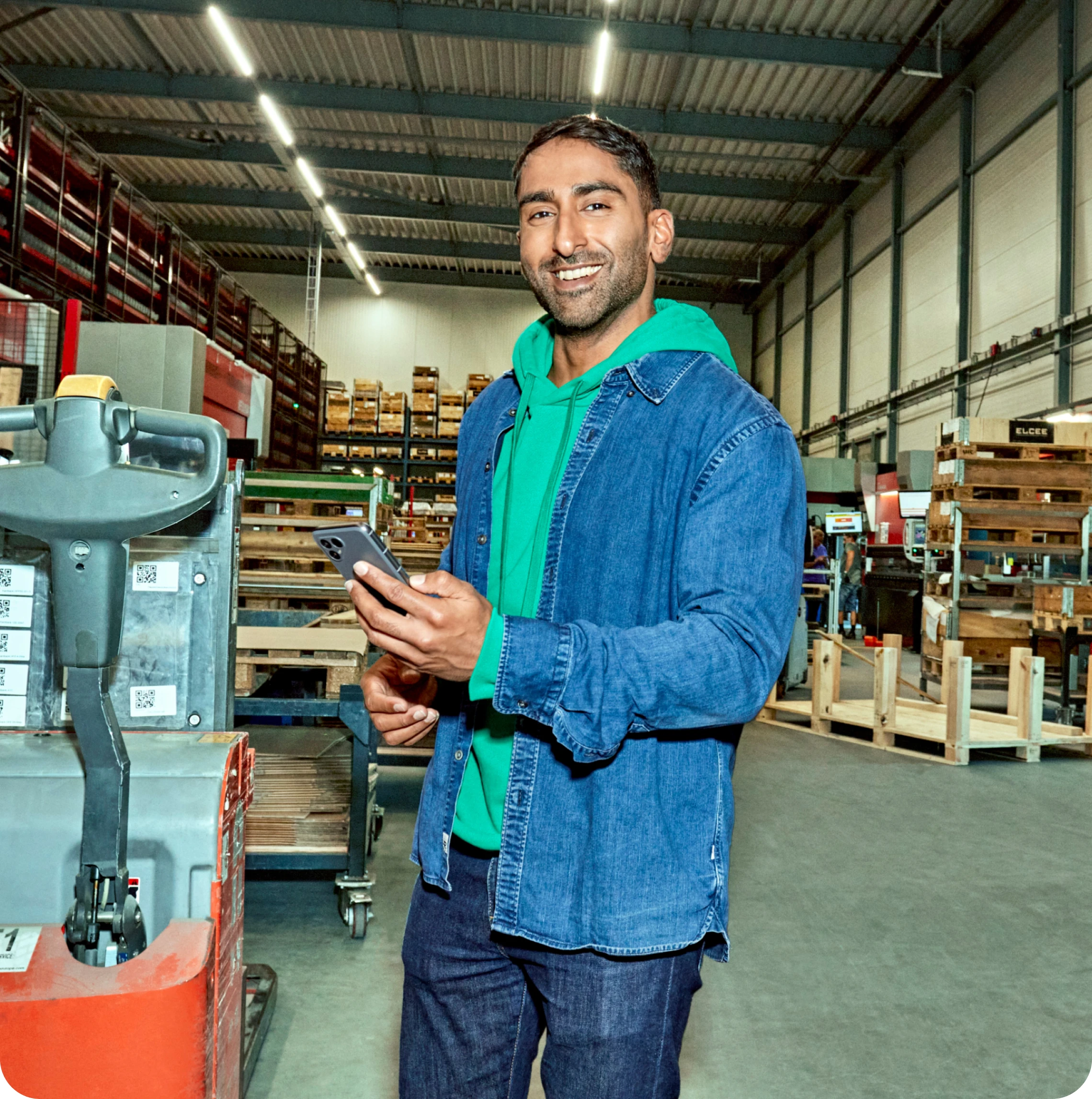 Man staat in een magazijn. Hij houdt een telefoon vast en lacht