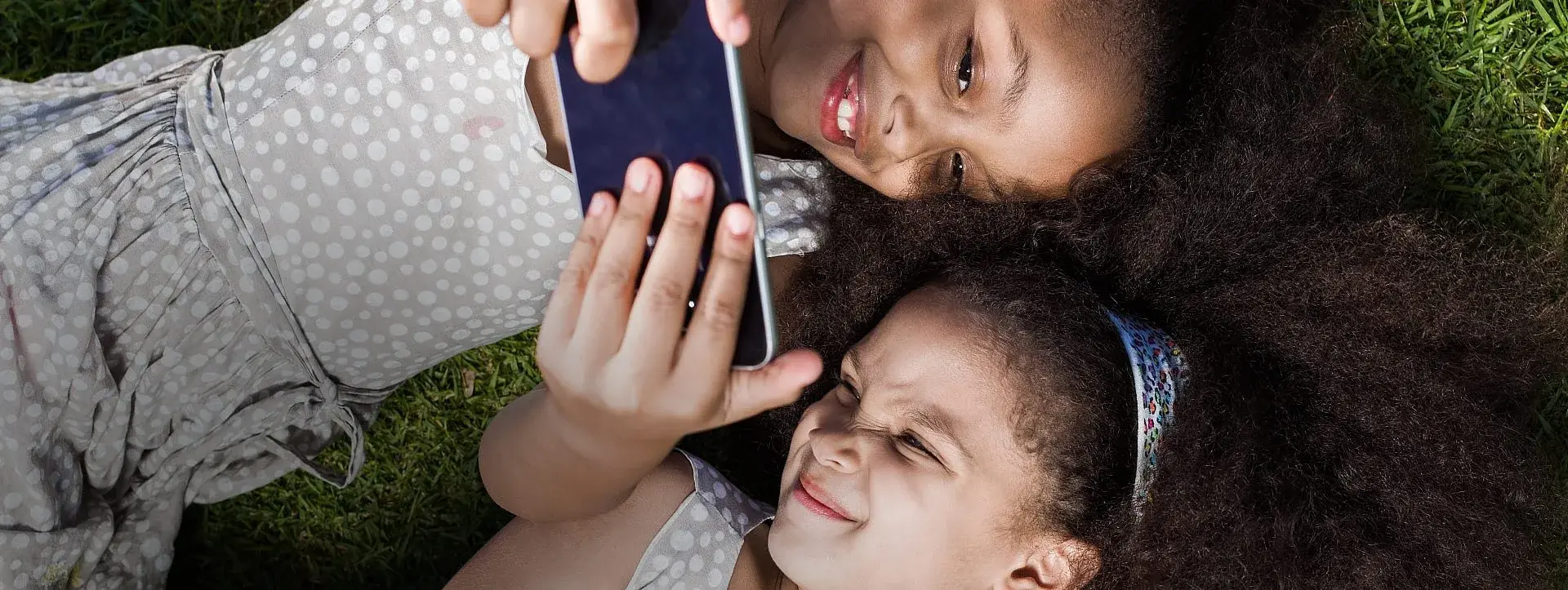 Kinderen kijken al liggend in het gras naar een telefoonscherm
