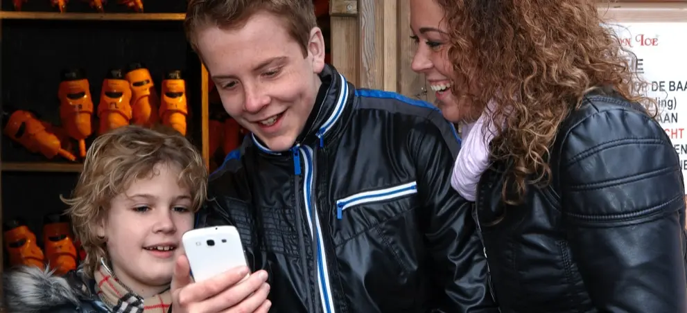 Moeder met 2 kinderen die lachend naar een mobiel kijken