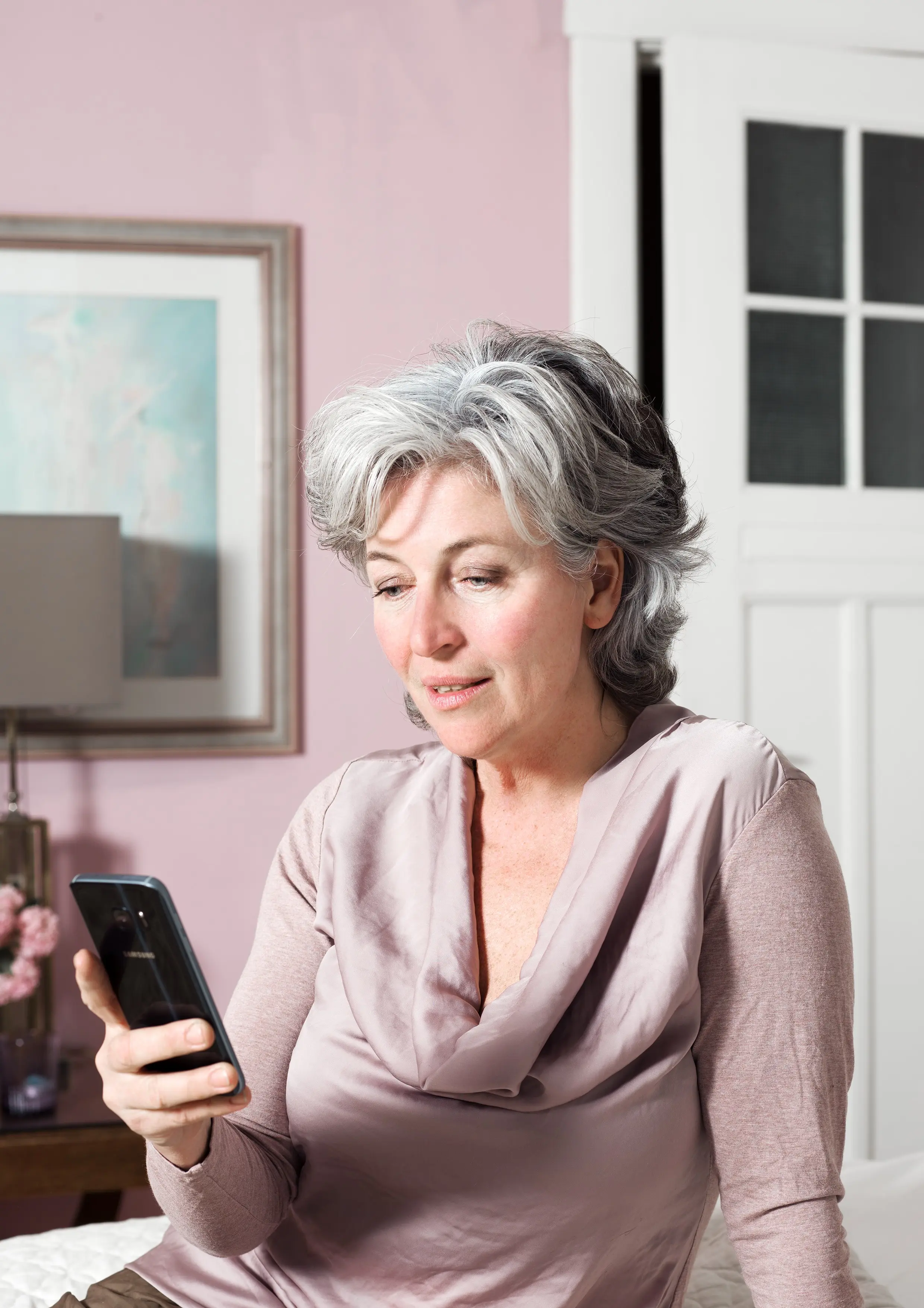 Grijsharige vrouw met haar mobiel in een woonkamer