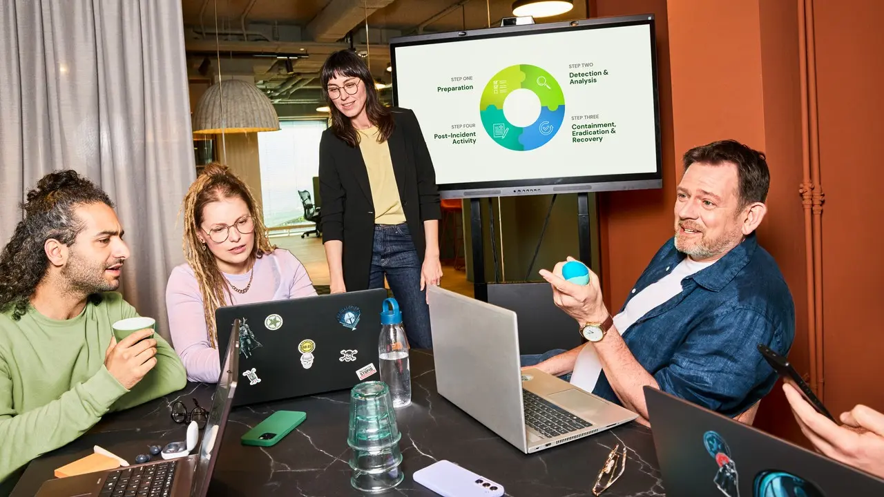 Drie collega's zijn in overleg op kantoor. Ze videobellen via de laptop.