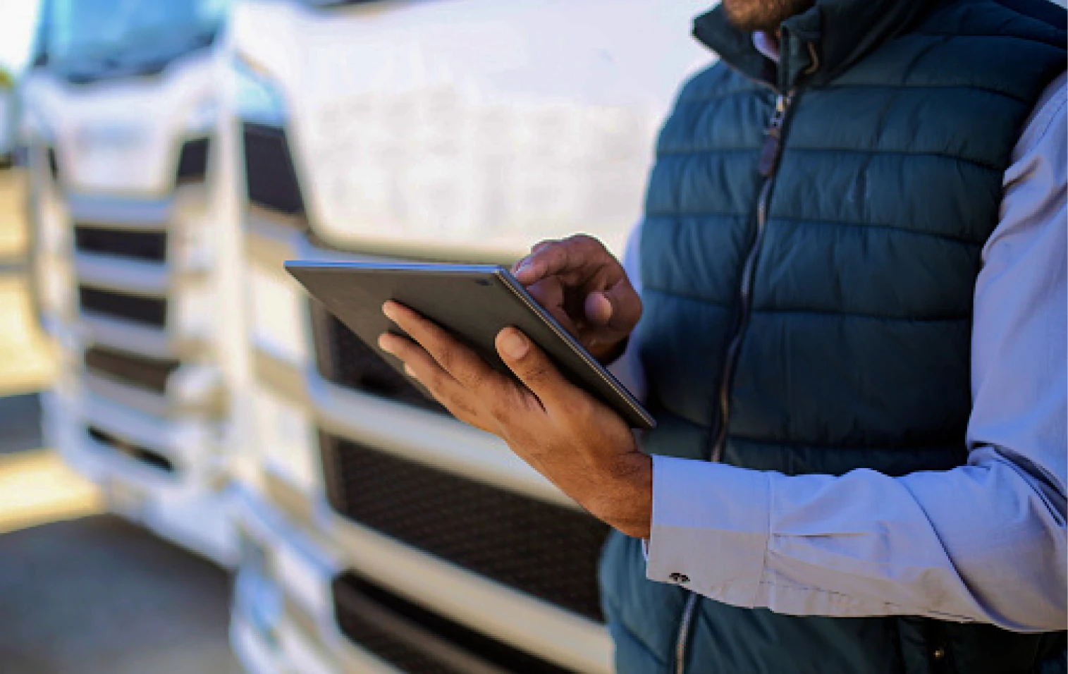 Man met bodywarmer staat tegen een vrachtwagen aan met een tablet in de hand