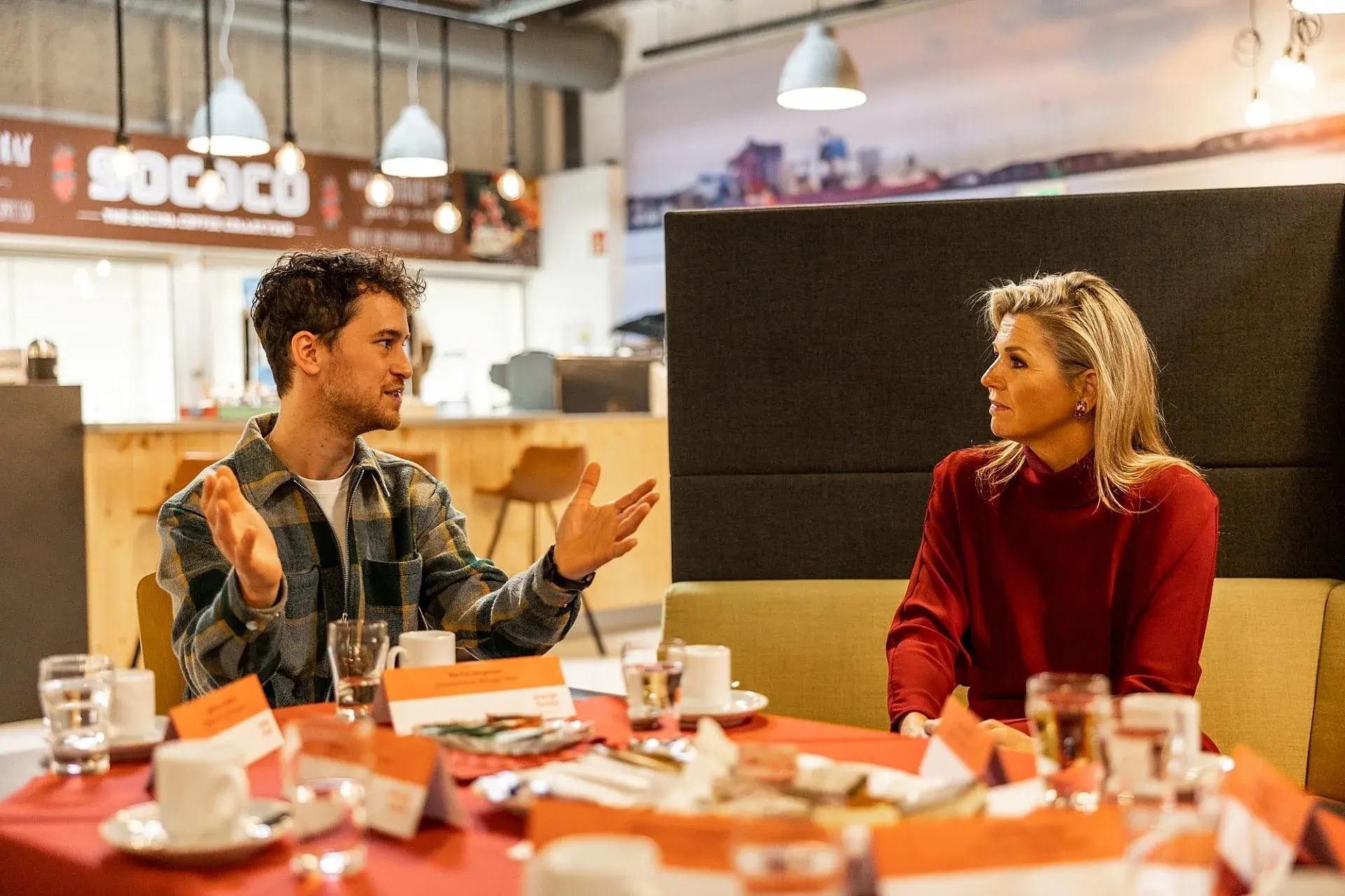 Koninging Maxima op bezoek bij KPN Mooiste Contact Fonds en Oranje Fonds, zittend aan een tafel in gesprek met meerdere mensen