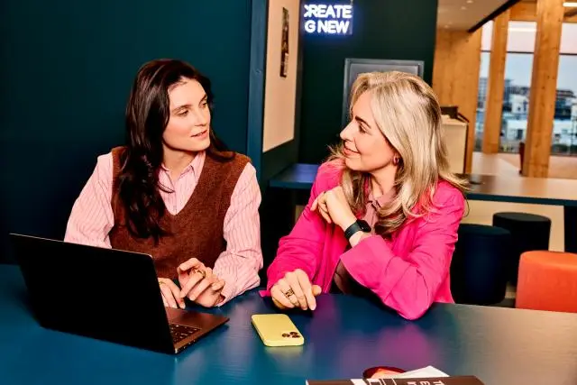 Twee vrouwen aan het werk. Ze zitten aan tafel en kijken samen naar het scherm van een laptop. 