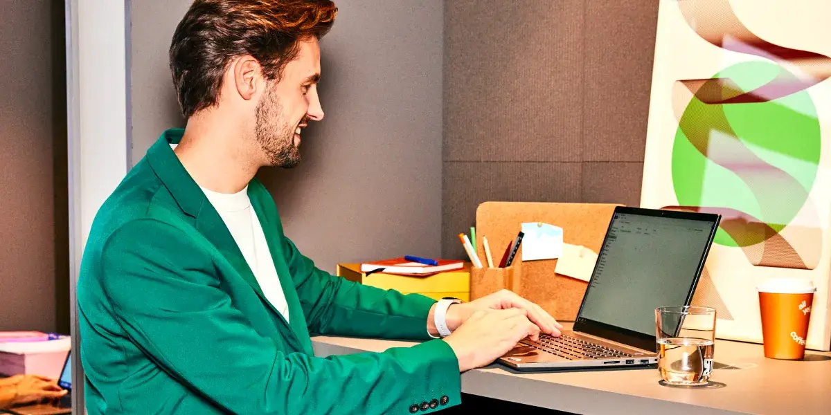 Een man in een groen pak werkt achter zijn bureau op een laptop.