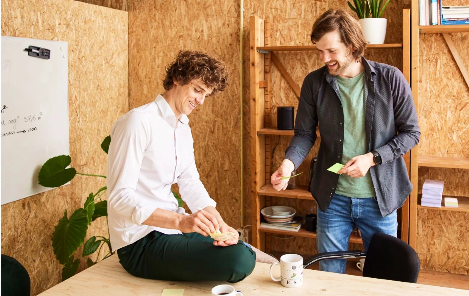 2 jonge mannen schrijven op post-its in een kantoor met muren van geperst hout