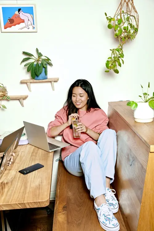 Vrouw zit met een drankje op een houten bank met haar laptop