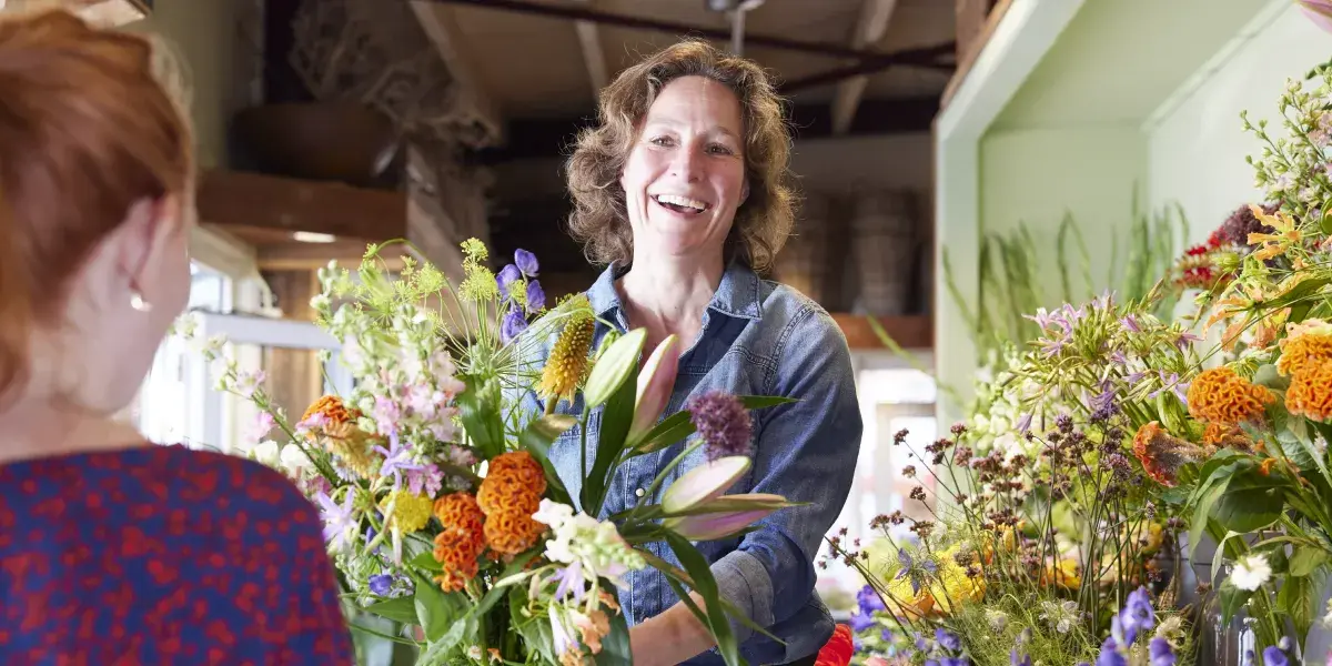 Verkoopster in bloemenzaak geeft een bos bloemen aan een klant