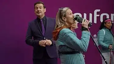 Rubn Nicolai en een vrouw bij een achterwand van Youfone, de vrouw is aan het zingen