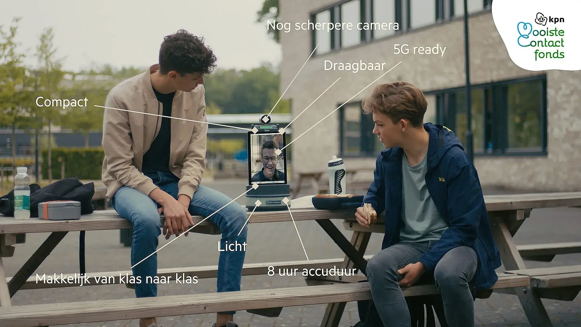 Twee jongens zitten buiten op picknick tafel met de KPN klasgenoot tussen hun in met de zieke in beeld