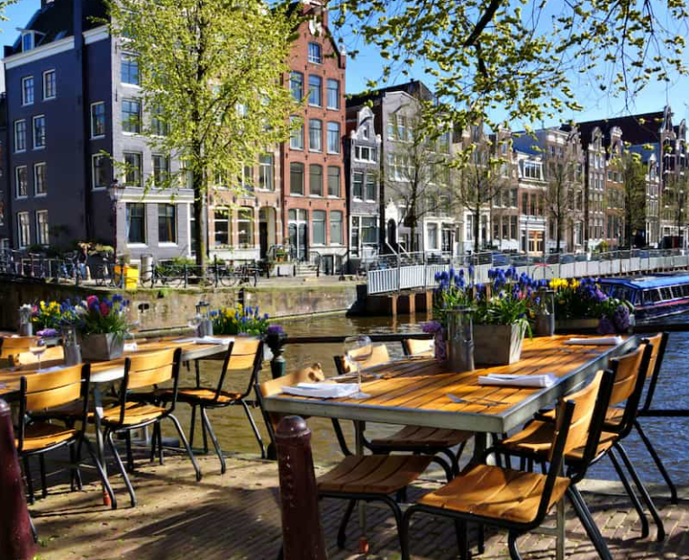 Een zonnig terras aan de gracht. Op de tafel staan glazen en bloemen.