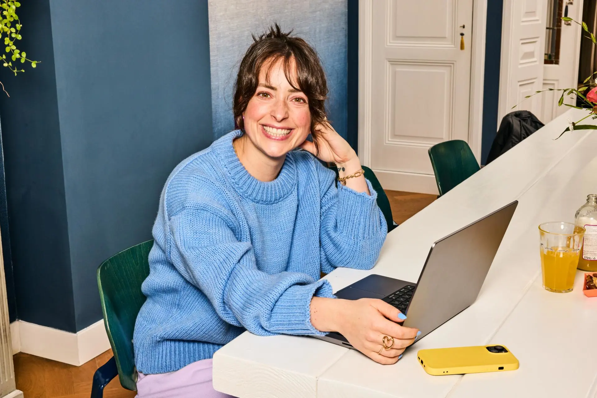 Vrouw met blauwe trui lachend achter laptop