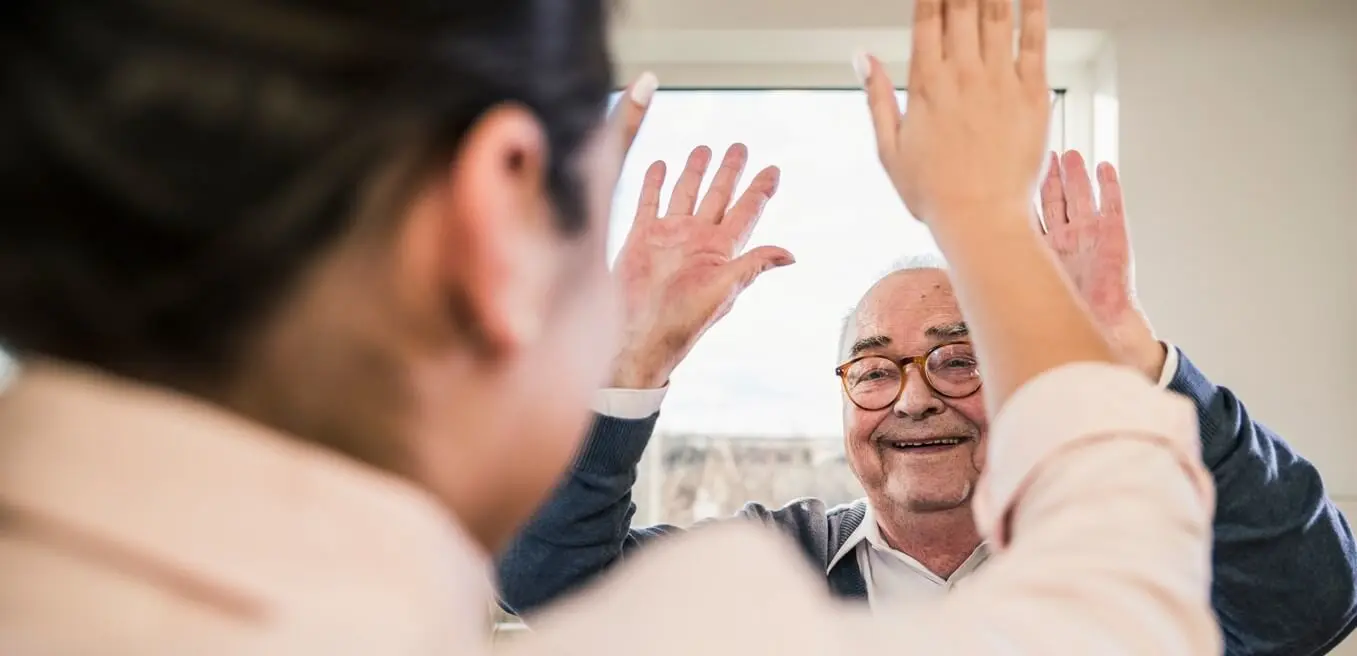 Een oudere man houdt beide handen in de lucht. Hij geeft de dame op de voorgrond een high five. 