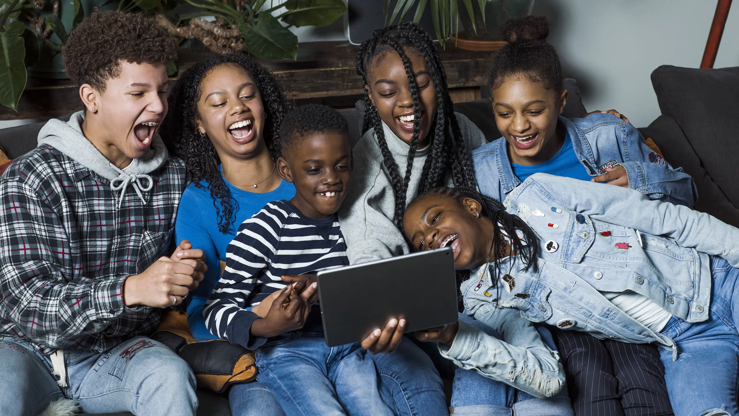 Een familie van 6 kinderen zitten samen lachend op de bank naar een tablet te kijken
