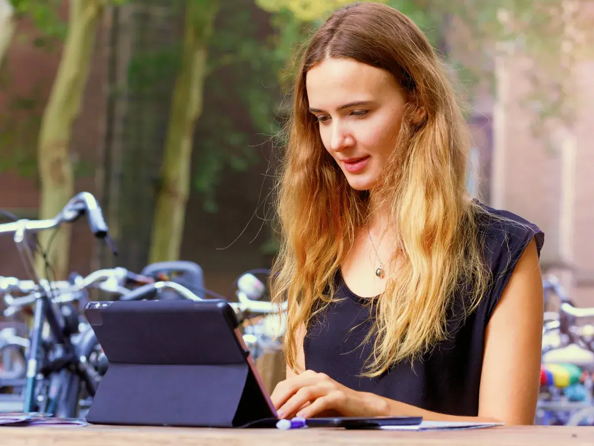 Een dame met lang blond haar werkt buiten op haar tablet.