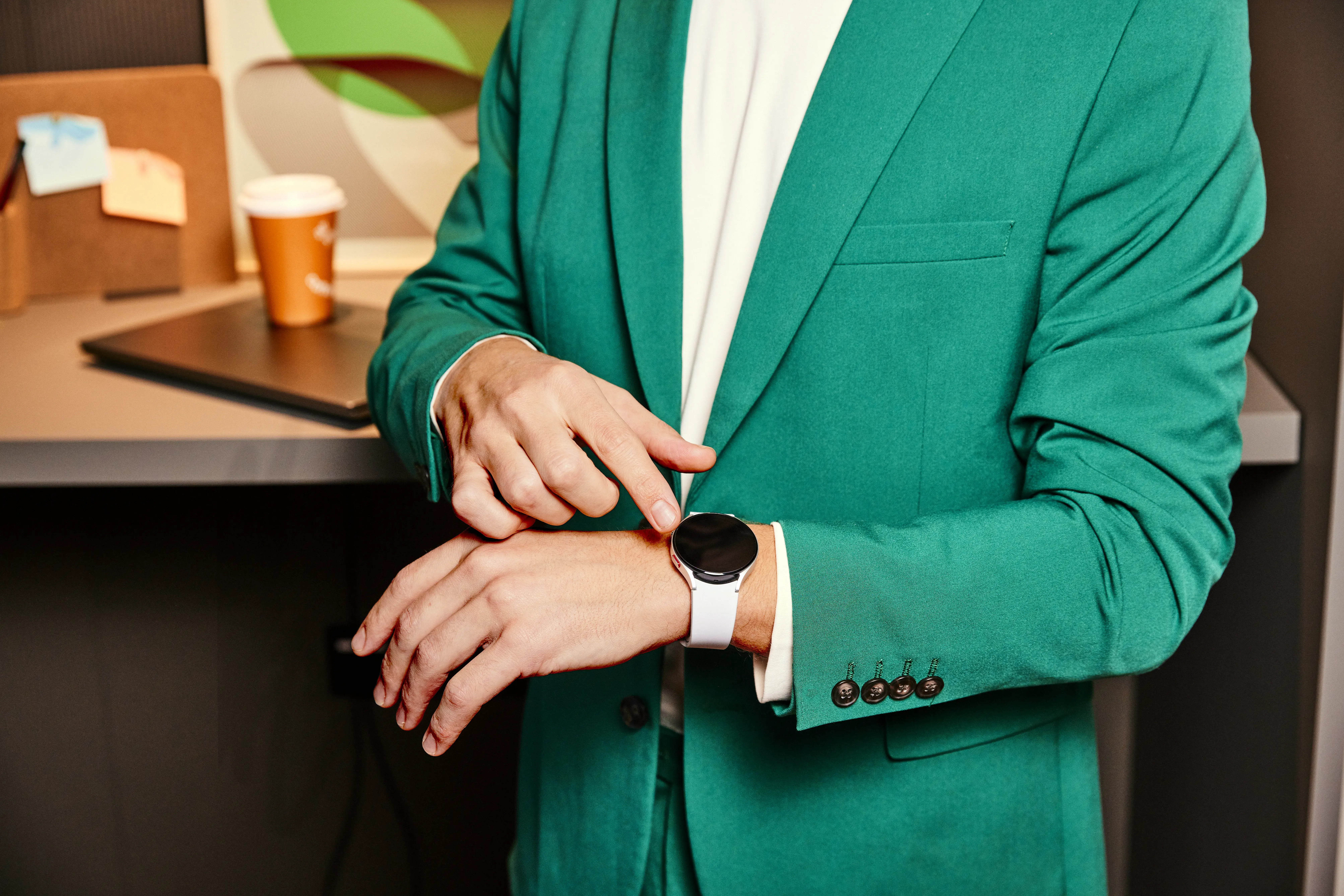 Een man met en smartwatch om zijn pols. Hij draagt een groen pak.